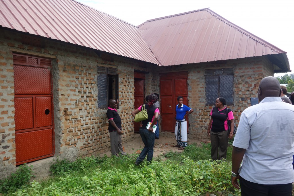 Safuroza a group member in a Blue T-shirt gives a site tour of her newly constructed house during an Soluti Finance East Africa board member visit in Bundibugyo.